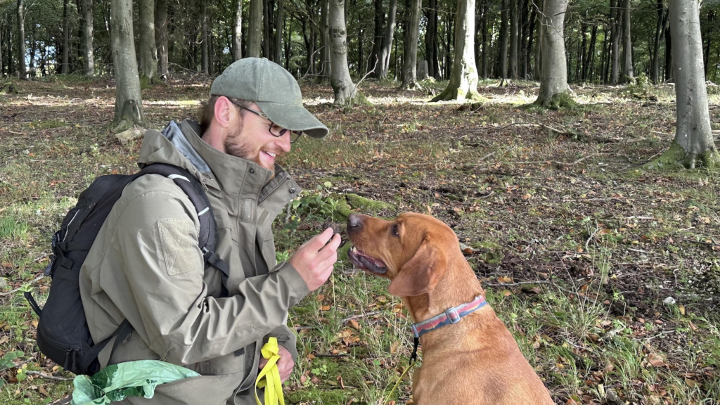 Ben holding a truffle up to Buddy's nose in the woods